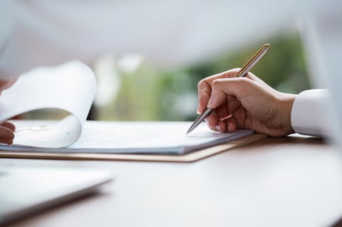 Close-up of a hand signing a business contract with a pen on a desk, symbolizing agreement and professional commitment