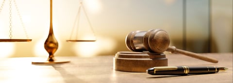 A close-up view of a golden balance scale, a wooden gavel on its block, and a fountain pen, symbolizing legal proceedings and fairness